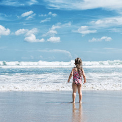 Naklejka premium Little girl standing on the beach and looking at the ocean. Bali. 