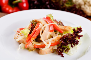 Salad with fried chicken breast, red bell pepper, onion and lollo rosso lettuce on white plate. Close up