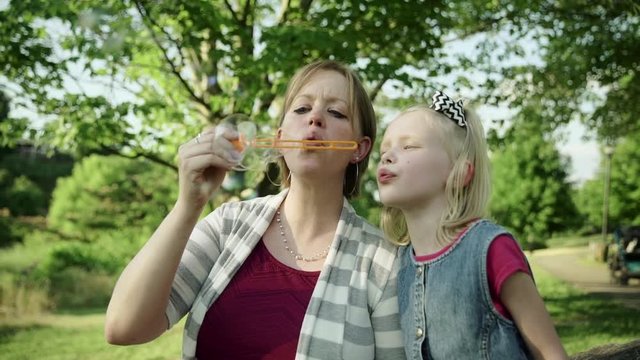Happy young mother and her daughter blowing soap bubbles in a summer park Slow motion Full HD