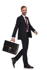 side view of cheerful businessman swinging his suitcase and walking