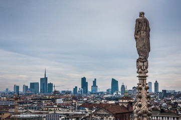 Fototapeta na wymiar Ancient statue on the roof of Duomo Milano with modern buildings on the background