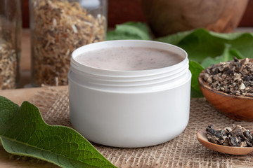 A jar of homemade comfrey root ointment with fresh symphytum plant