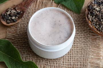A jar of homemade comfrey root ointment with fresh symphytum plant