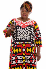 Studio shot of fat black African woman standing while holding gl