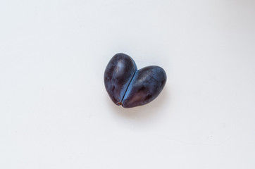 Heart shaped ripe plum on a white table. 