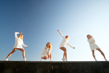 Multiplied collage of young redgead dancing girl, weared in white dress and sneakers, white blue sky background