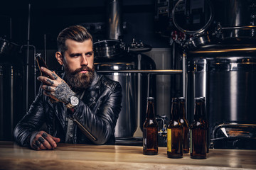Stylish bearded biker dressed black leather jacket sitting at bar counter in indie brewery.