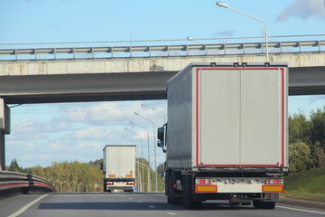 Road transport - white trucks with semi-trailers go under the bridge drive the suburban asphalt...