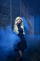 girl in a black short dress with white long wavy hair on a dark brown and black background with a smoke bomb and blue smoke