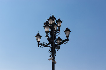 Fototapeta na wymiar Church bronze multi lamppost against blue sky. Orthodox crosses on the lanterns. Many black lanterns on one post.