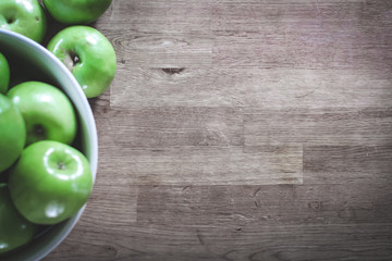 Green granny smith apples in a white bowl on a butcher block counter - Powered by Adobe