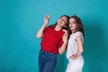 Full height image of two happy cheeky girls , best friends having fun , laughing on blue background. . Wearing stylish casual clothes. Space for text. Cute teenage school girls