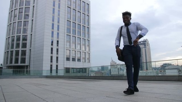 Relaxed joyful african american businessman taking break and giving himself minutes of joy while dancing afrobeat style outside office building. Successful executive in afrohouse dance on city street.
