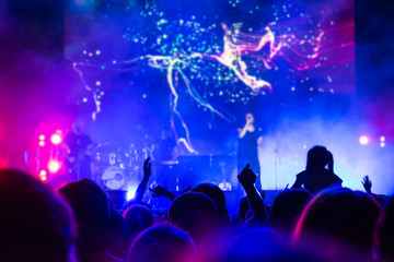 Fototapeta na wymiar Crowd at concert. People silhouettes on backlit by bright blue and purple stage lights. Cheering crowd in colorful stage lights. Raised hands and smartphones against scene