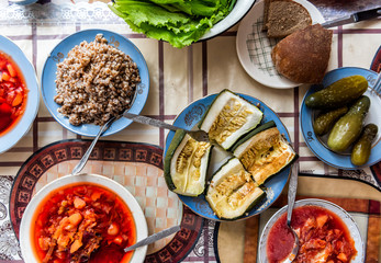Flat top, high angle view down of table with setting of healthy vegan vegetarian lunch or dinner, green vegetables, salad, pickled cucumbers pickles, traditional beet borscht soup