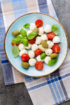 Delicious caprese salad with ripe cherry tomatoes and mini mozzarella cheese balls with fresh basil leaves.