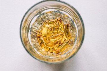 Glass of fish oil capsules on gray background