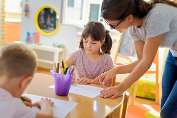 Preschool teacher assisting children with their drawings. Early education. Harnessing creativity...