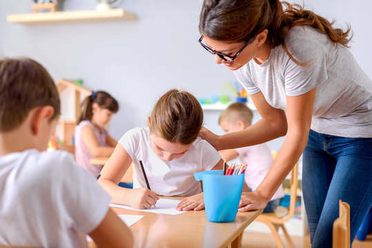 Preschool teacher assisting children with their drawings. Early education. Harnessing creativity and support.