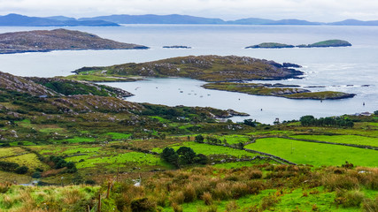 Fototapeta na wymiar view of green fields, rocky shore and bay facing the Dingle Peninsula across the water while driving along the Ring of Kerry