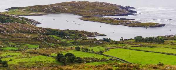 view of green fields, rocky shore and bay  while driving along the Ring of Kerry