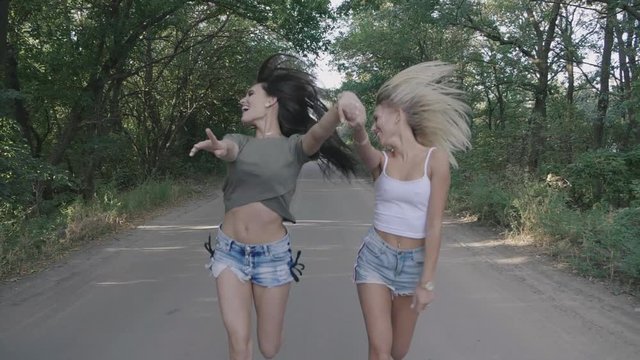 Two best friends sexy hot girls runnung and having fun together on a road at forest or park.