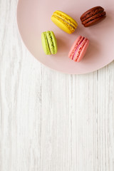 Sweet and colorful macarons on a pink plate over white wooden background, top view. Closeup. Copy space.