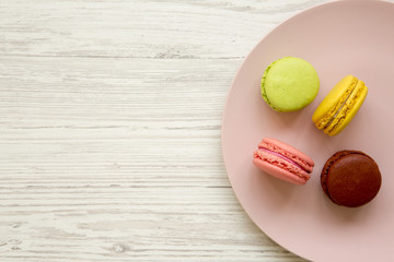 Colorful macaroons on a pink plate over white wooden background, overhead view. Close-up. Copy space.