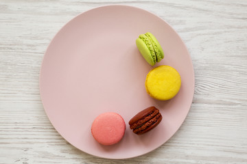 Sweet and colorful macaroons on a pink plate over white wooden surface, top view. Closeup.