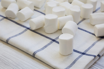 Fototapeta na wymiar Closeup of sweet white marshmallows on cloth over white wooden background. Side view.