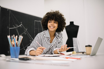 Curly dark skinned fashion designer planning working process at workplace. Successful business....