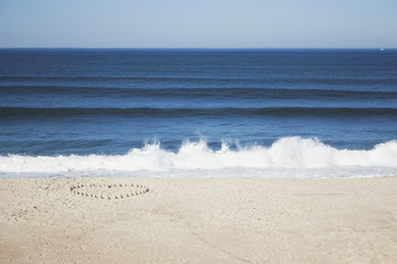 Heart in the sand made of tiny sandcastle towers, in bright sunny day at beach with a blue ocean. With copy space.