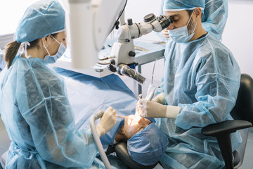doctor operating man in cabinet with eyes closed during procedure made by dentist and assistant.