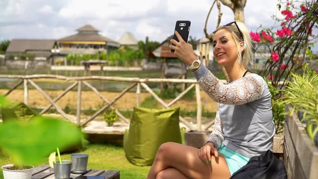 Young woman taking selfie photo with smartphone in garden cafe