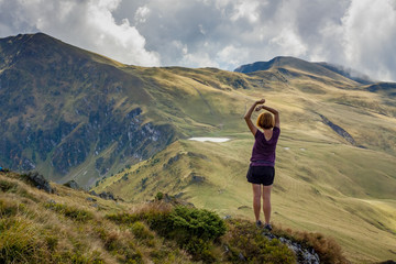Naklejka na ściany i meble Girl in violet t-shirt standing on the stone and looking at mountain ridge