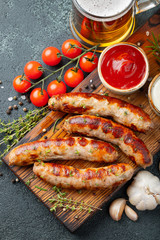 Fried sausages with sauces and herbs on a wooden serving Board. Great beer snack on a dark background. Top view
