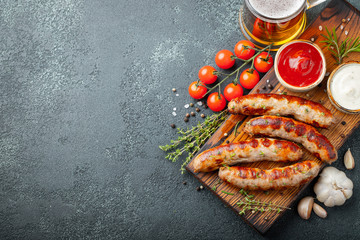 Fried sausages with sauces and herbs on a wooden serving Board. Great beer snack on a dark background. Top view with copy space