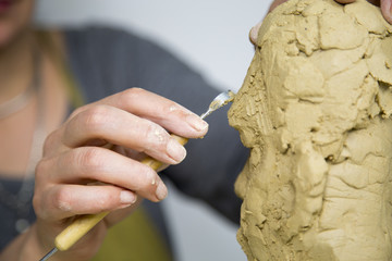 Sculptor artist creating a bust sculpture with clay. She is happy of her work, she is concentrated, she is sculpting a woman. the statue is at foreground. Sculptor at work.