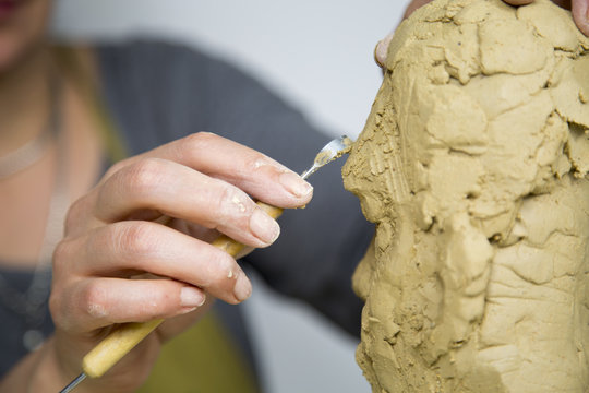 Sculptor artist creating a bust sculpture with clay. She is happy of her work, she is concentrated, she is sculpting a woman. the statue is at foreground. Sculptor at work.