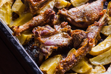Baked meat with potatoes. Duck meat with golden crust on baking sheet. Cooked in oven dish on parchment. Golden sliced potatoes with chicken meat. Home kitchen