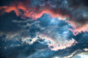 A stormy sky with a bright red glow. Colorful image of dramatic cloudscape. Amazing clouds of pink, white, gray color on the background of the evening dark sky after sunset.