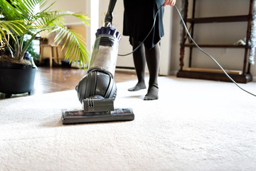Closeup of woman, female doing cleaning at home with vacuum cleaner showing head, brush on carpet...
