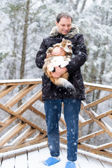 Closeup of young man holding angry, scared meowing maine coon cat outside, outdoors in park in snow, snowing weather during snowstorm, storm with snowflakes, flakes falling