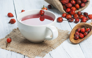 Dried rose hip cup of herbal tea medicinal plants on white black wooden table with wooden shovel and rosehips in burlap sack. Dogrose background