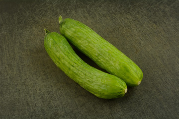 Two whole raw freshly rinsed Persian cucumbers on black cutting board