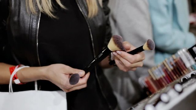 Close up of young woman choosing powder brush at cosmetic shop, testing before buying