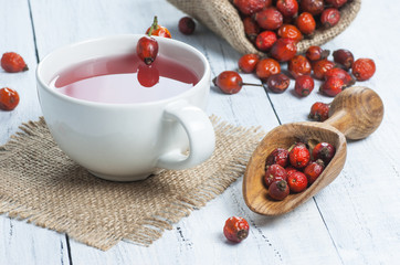 Dried rose hip cup of herbal tea medicinal plants on white black wooden table with wooden shovel and rosehips in burlap sack. Dogrose background