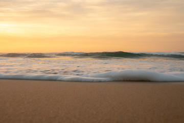 Fototapeta na wymiar Orange sunrise and small foamy waves at the beach
