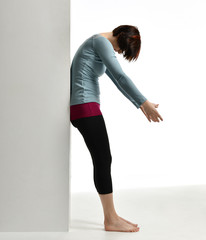 Woman exercising doing postnatal workout. Female fitness instructor stretching her spine near wall in gym work out exercises