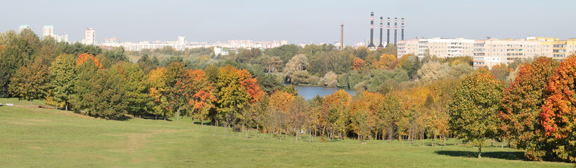 Panoramic view of autumn park with deciduous trees that began to turn red and yellow on shore of lake. Minsk, Belarus